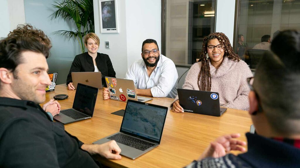 a group of people sitting at a table with laptops webhook